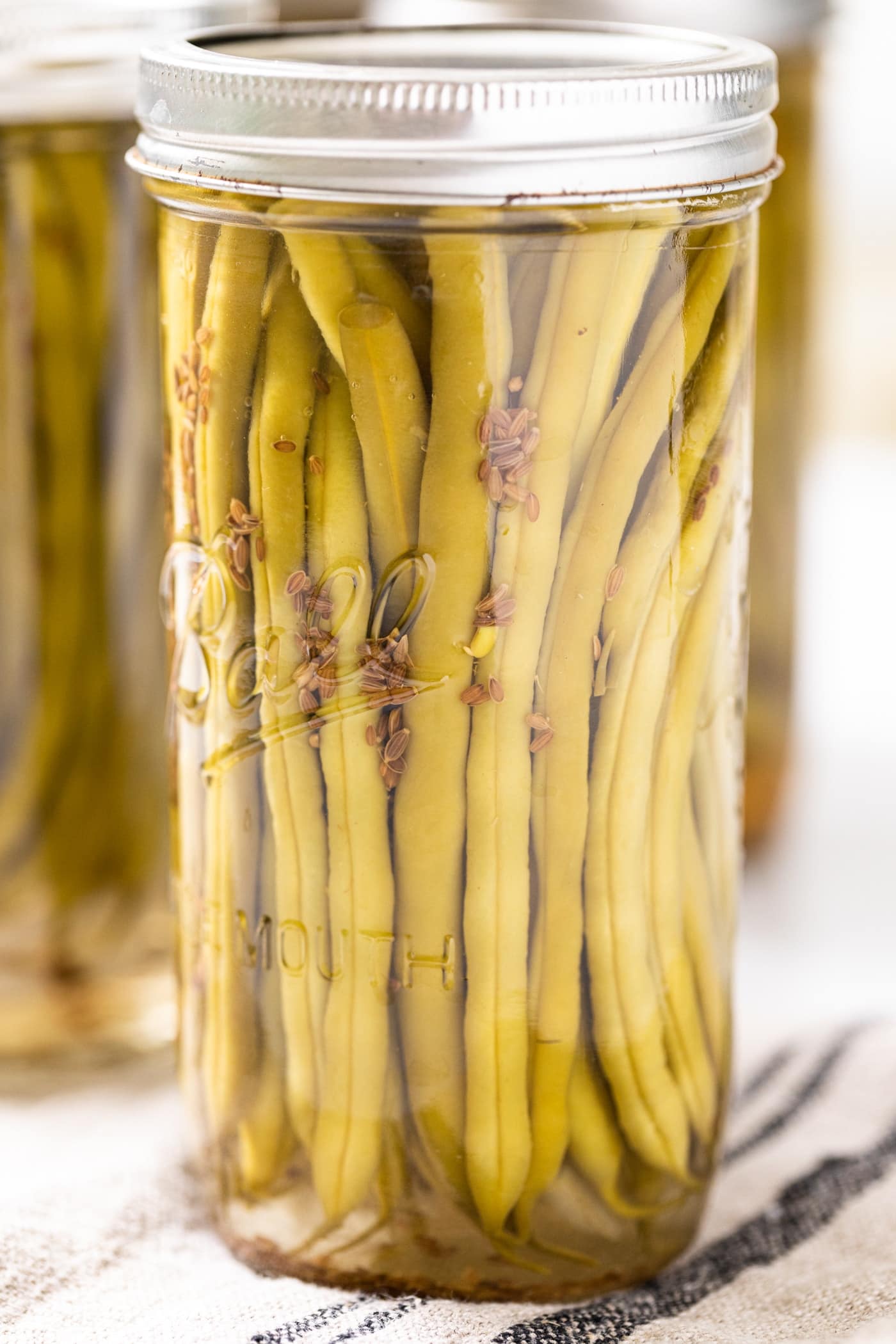Close up view of glass canning jar filled with green beans with dill seeds floating down the side toward the bottom of the jar