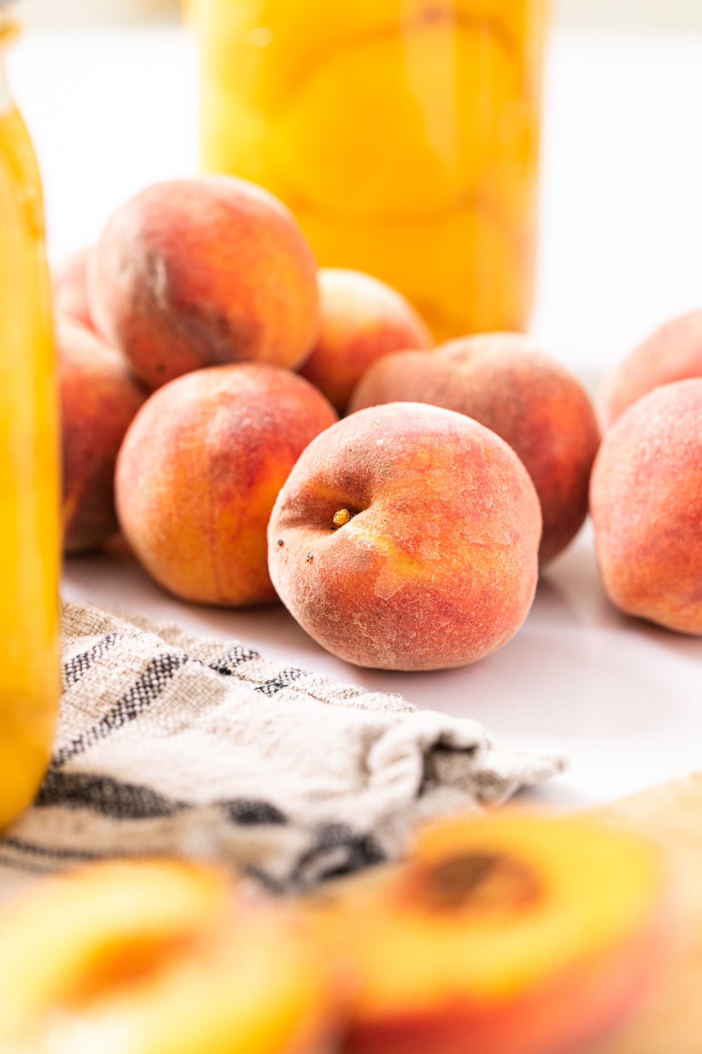 Unsliced peaches sitting on white countertop with glass jars filled with peaches