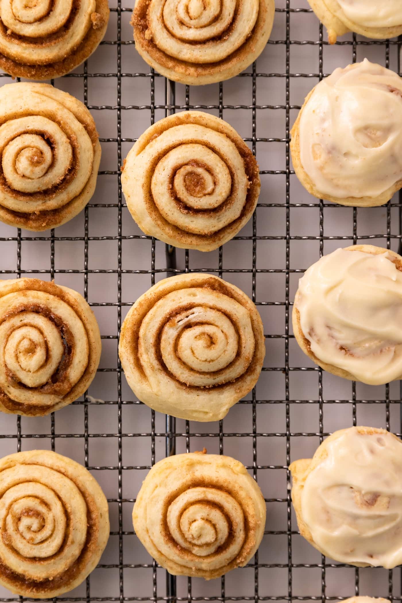 Top down view of little cinnamon roll cookie swirls some with white frosting all sitting on wire cooling rack