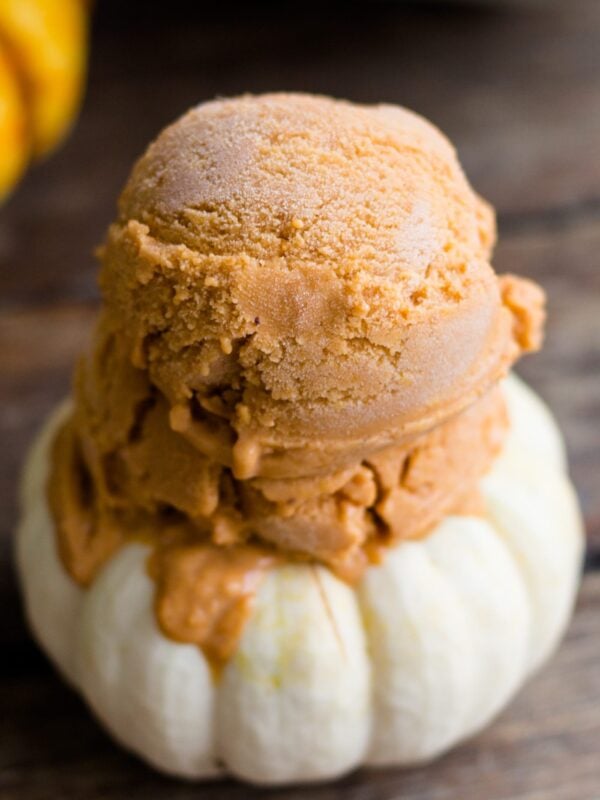Frozen pumpkin custard scooped onto a small white pumpkin with yellow and white pumpkins in background on a wood surface