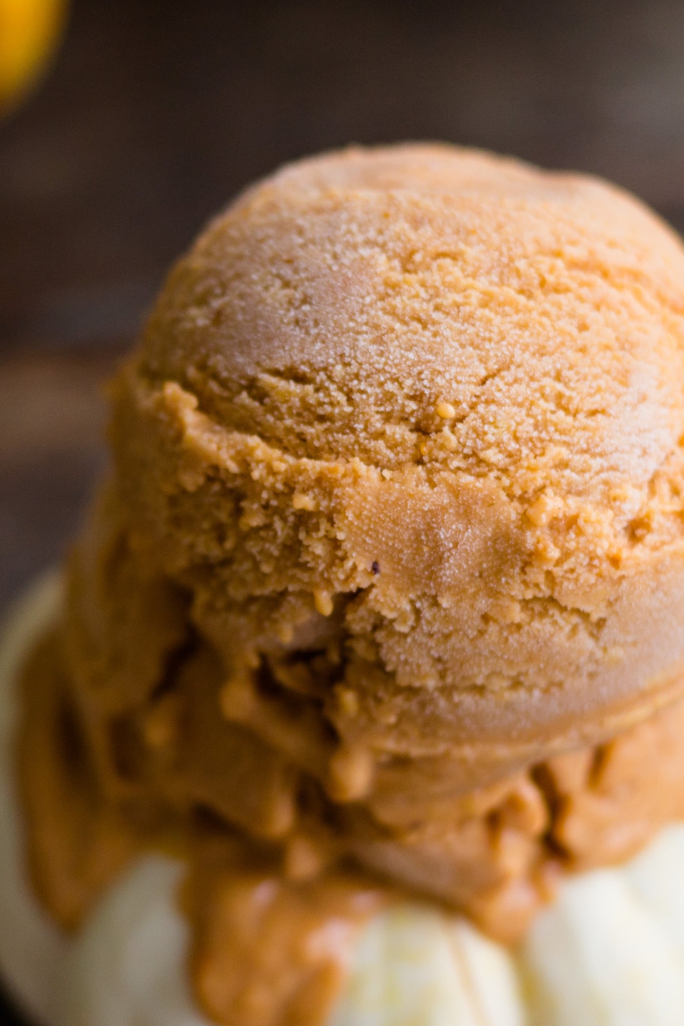 Frozen pumpkin custard scooped onto a small white pumpkin with yellow pumpkin in background on a wood surface