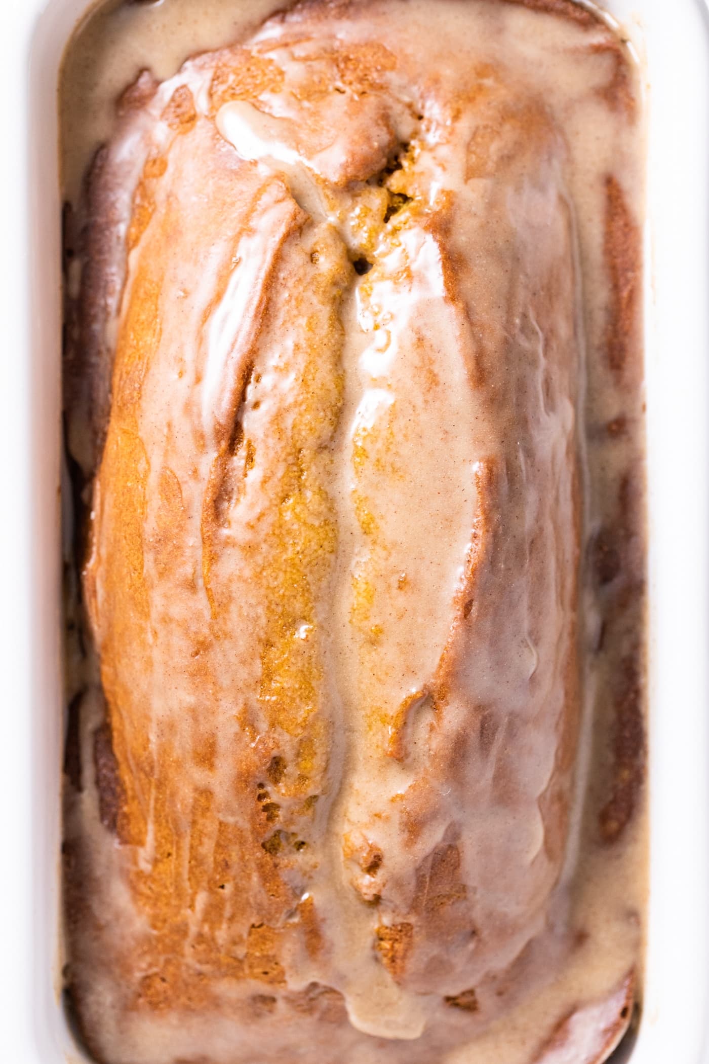 Top down view of top of brown colored pumpkin loaf bread sitting in white pan