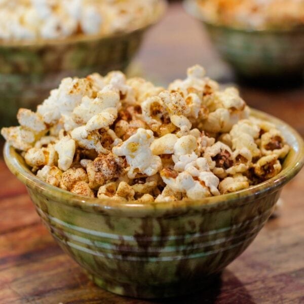 Green speckled bowl full of kettle corn sitting on wood surface with two bowls full of popcorn in background