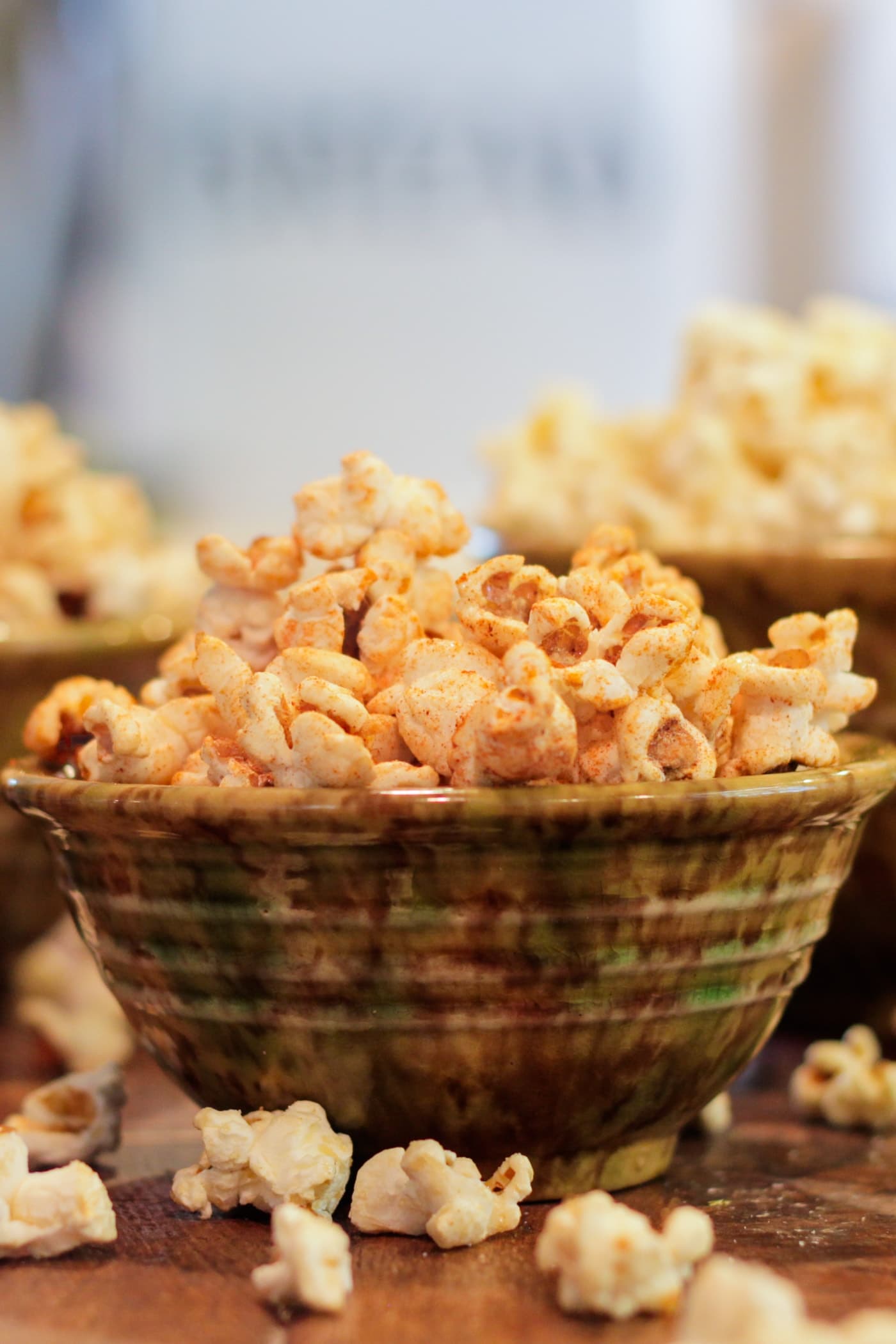 Green speckled bowl filled with kettle corn sitting on wood surface with extra bowls of popcorn in background and popcorn pieces sprinkled about