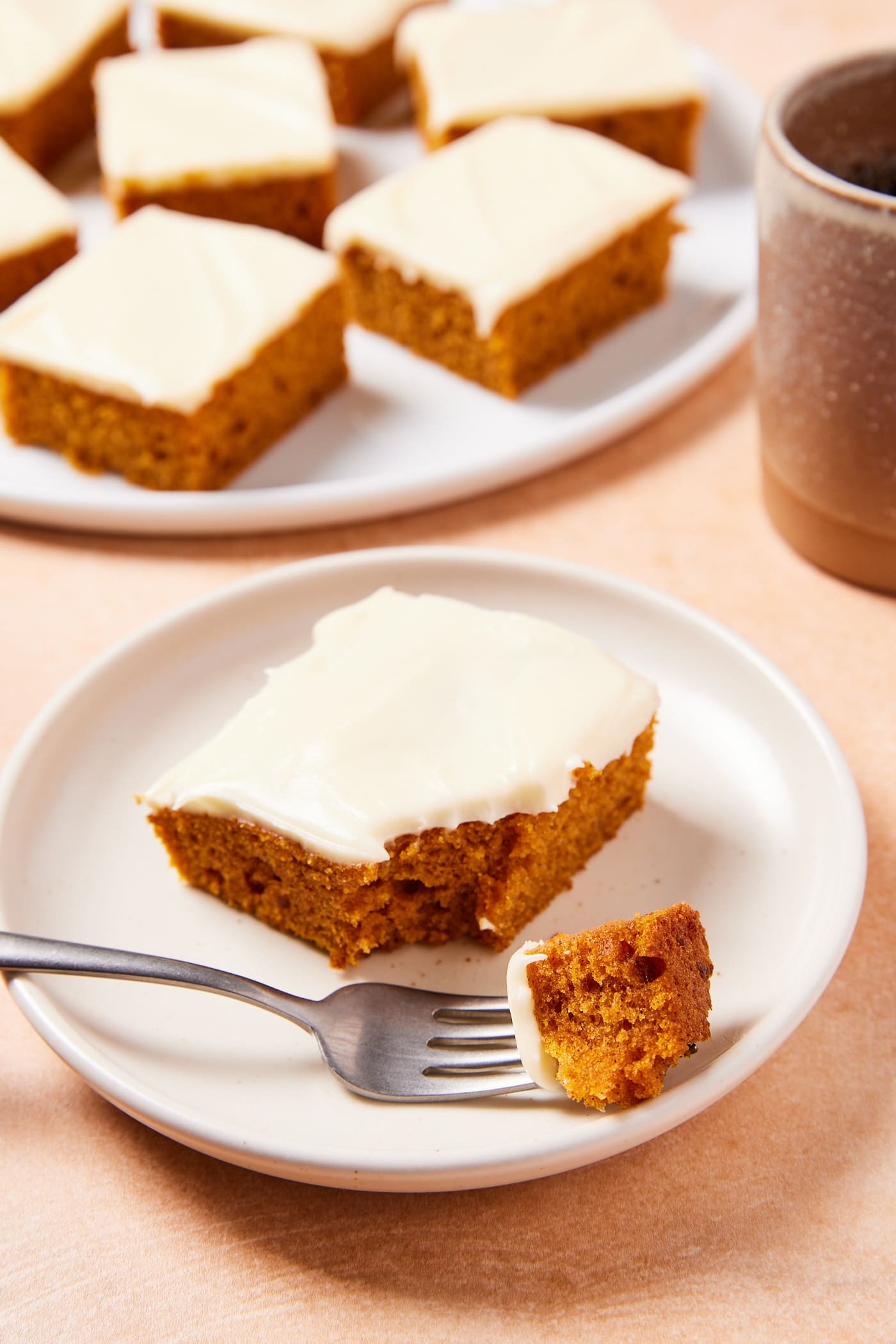 White plate with square of pumpkin bar with fork taking a piece from the cake.