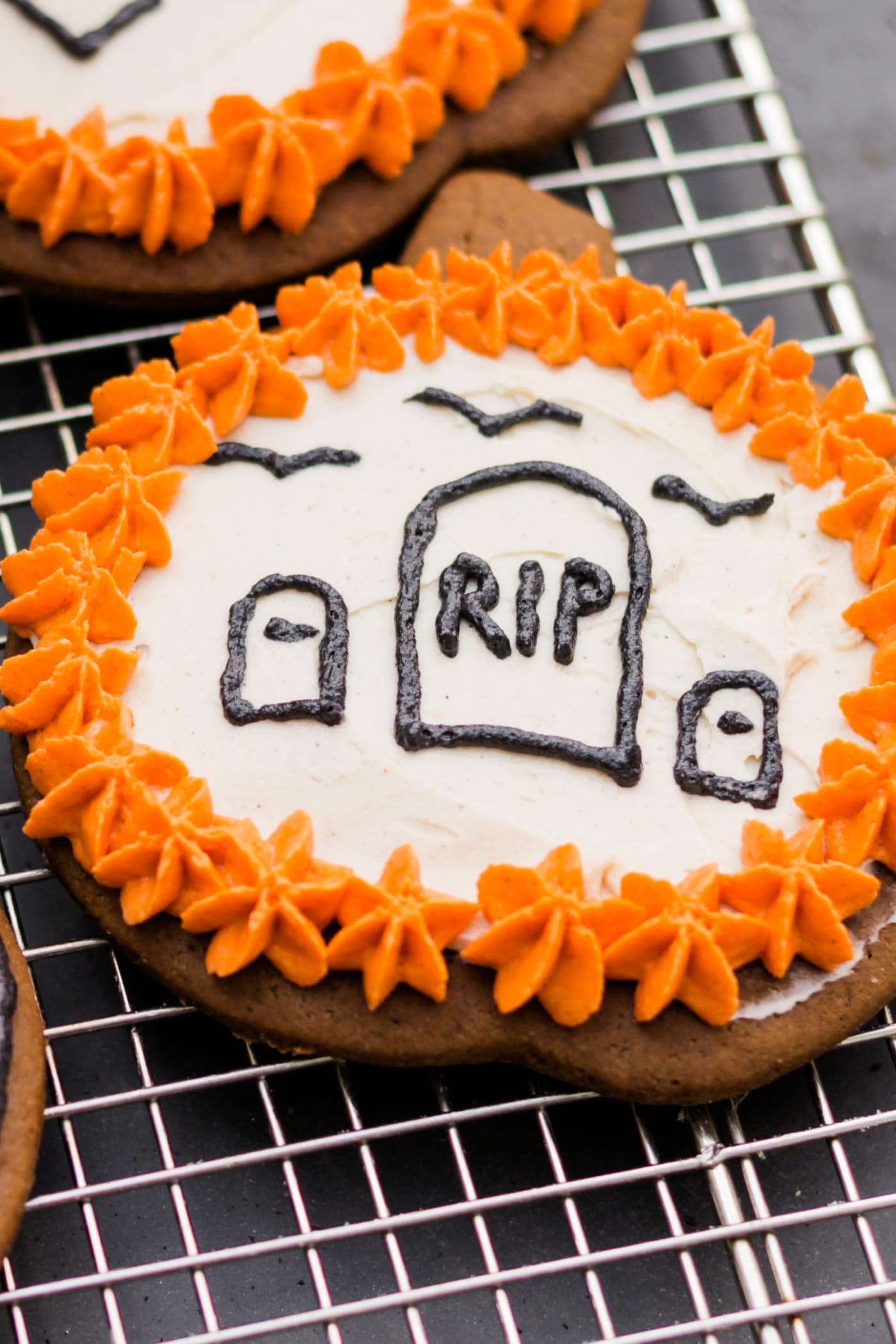 Spiced ginger cutout cookies topped with orange and white frosting sitting on wire cooling rack with extra cookie in background