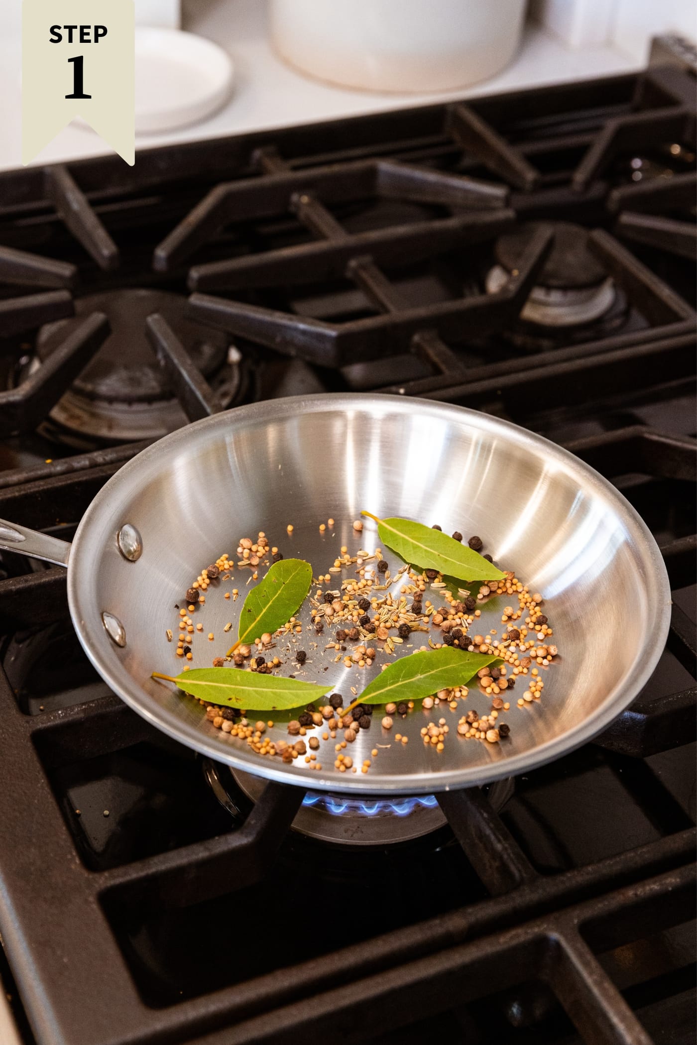 Metal skillet on stovetop filled with toasting spices and bay leaves.