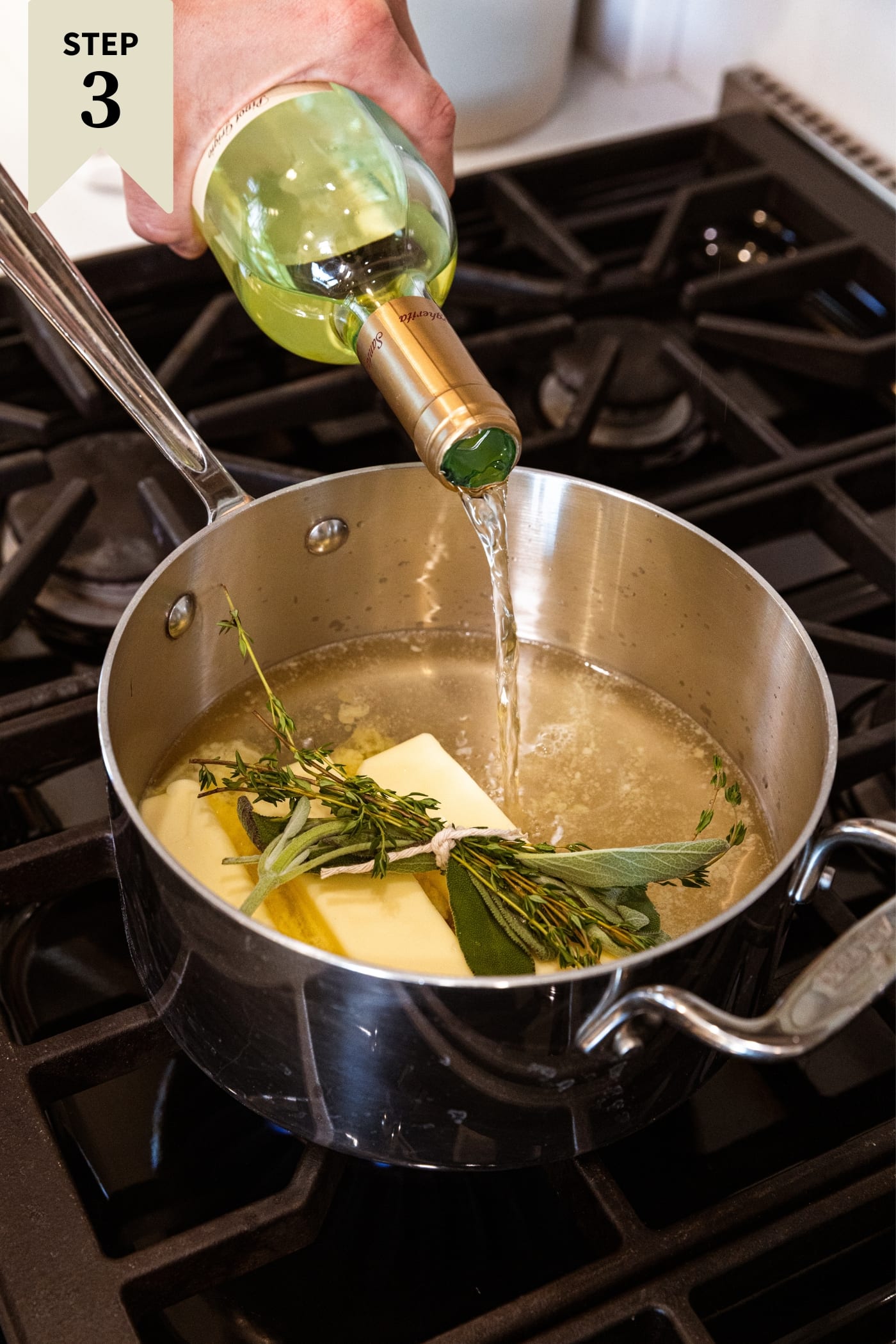 Bottle of white wine being poured into a metal kettle with packet of herbs tied together along with three sticks of unmelted butter.