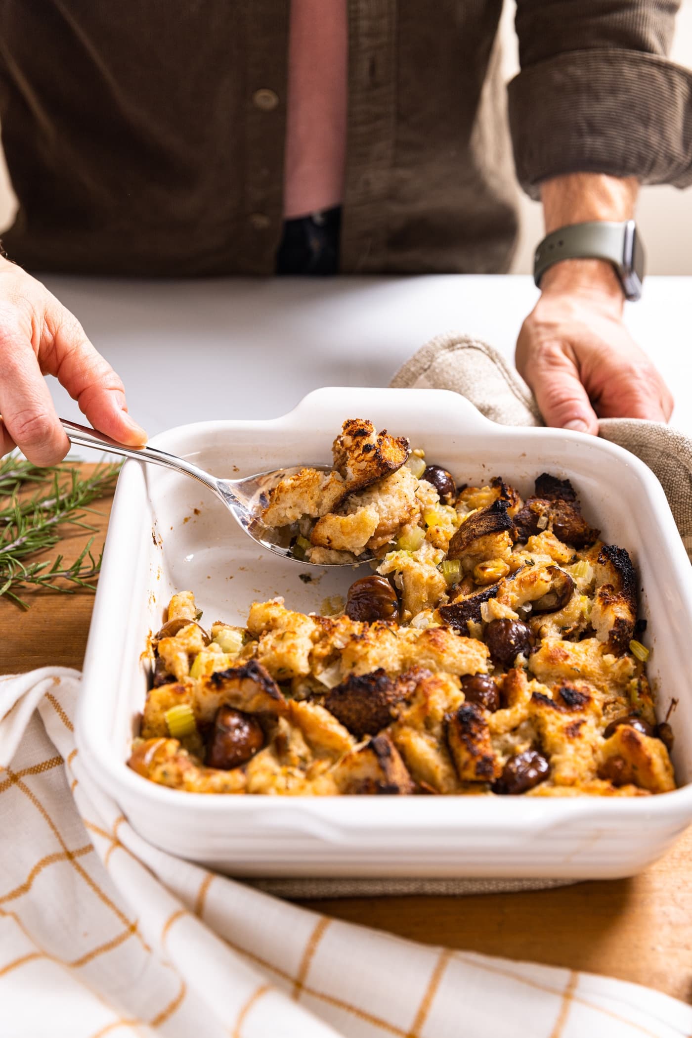 Hand spooning out serving of slow cooker stuffing out of white baking dish all on white countertop