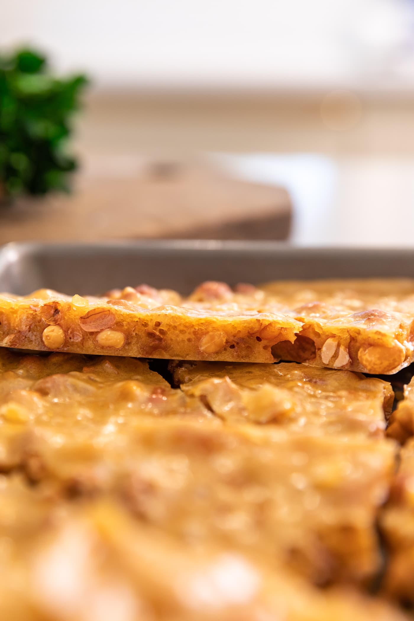 Side view of yellow piece of peanut brittle showing airy pockets with peanuts showing as well sitting on top of other pieces of brittle