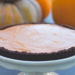 Round cake plate with pumpkin tart with chocolate crust on top with pumpkins in background.