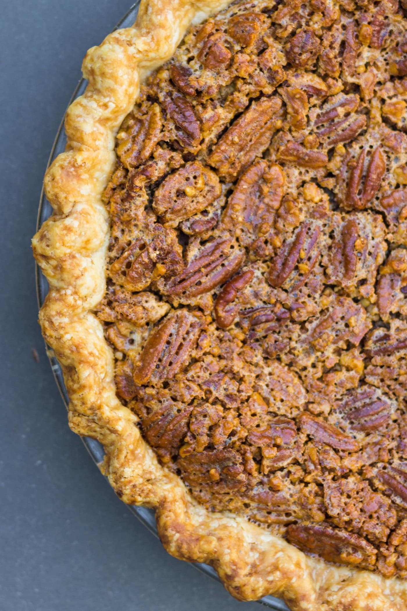Top down view of pecan pie with pieces of pecans on top and browned crust all on blue slate surface
