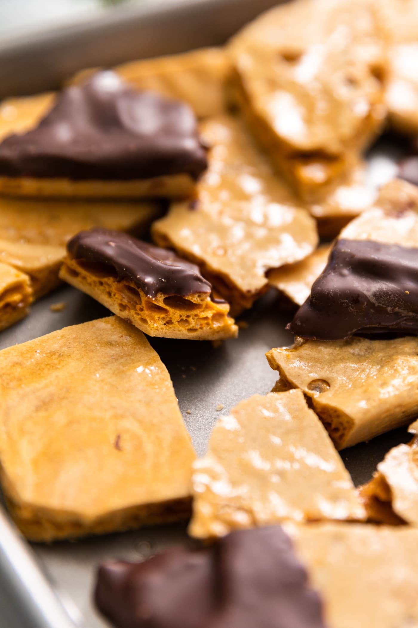 Pieces of sponge candy sprinkled around baking sheet, some with chocolate on top, and showing the sponge-like interior of pieces