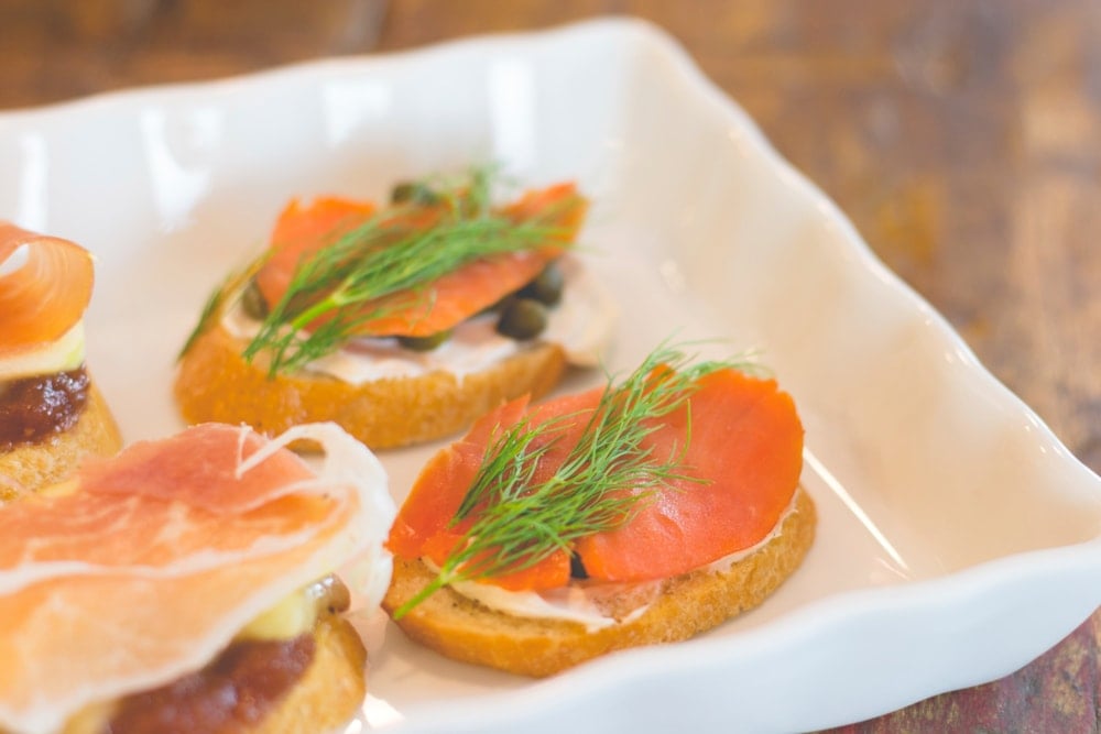 Crostini topped with smoked salmon and sprigs of dill sitting on white serving platter