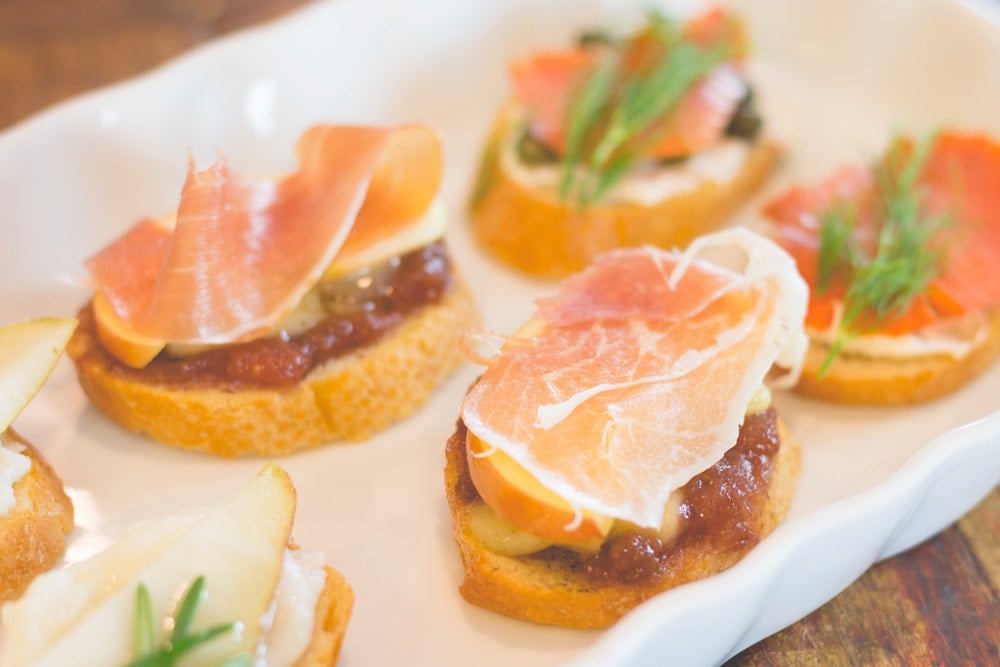 Crostini with prosciutto and apple and fig sitting on white serving platter