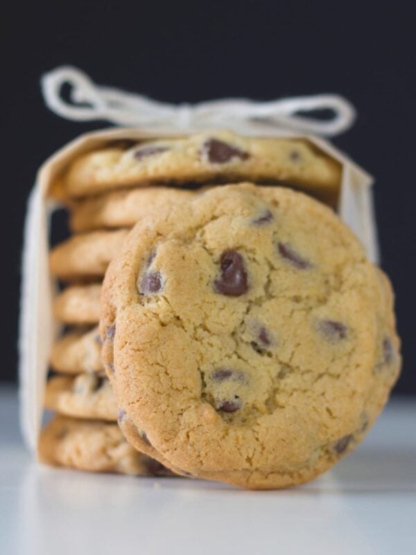 Stack of chocolate chip cookies sitting on white countertop with parchment and bow on top wrapping them up