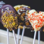Lots of chocolate pops made from different types of chocolate topped with various different toppings including nuts and sprinkles