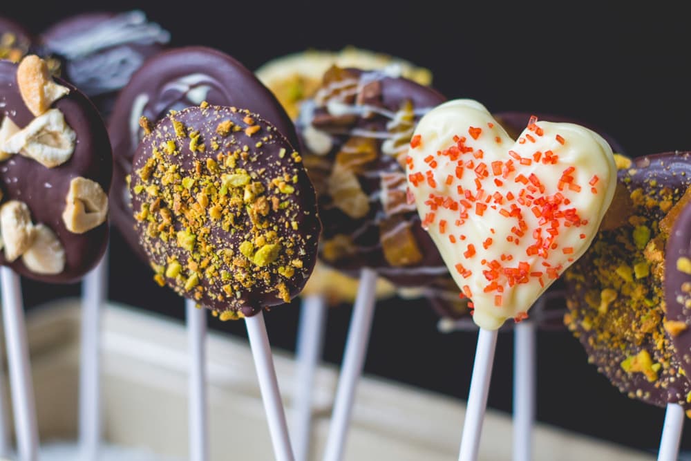 Lots of chocolate pops made from different types of chocolate topped with various different toppings including nuts and sprinkles