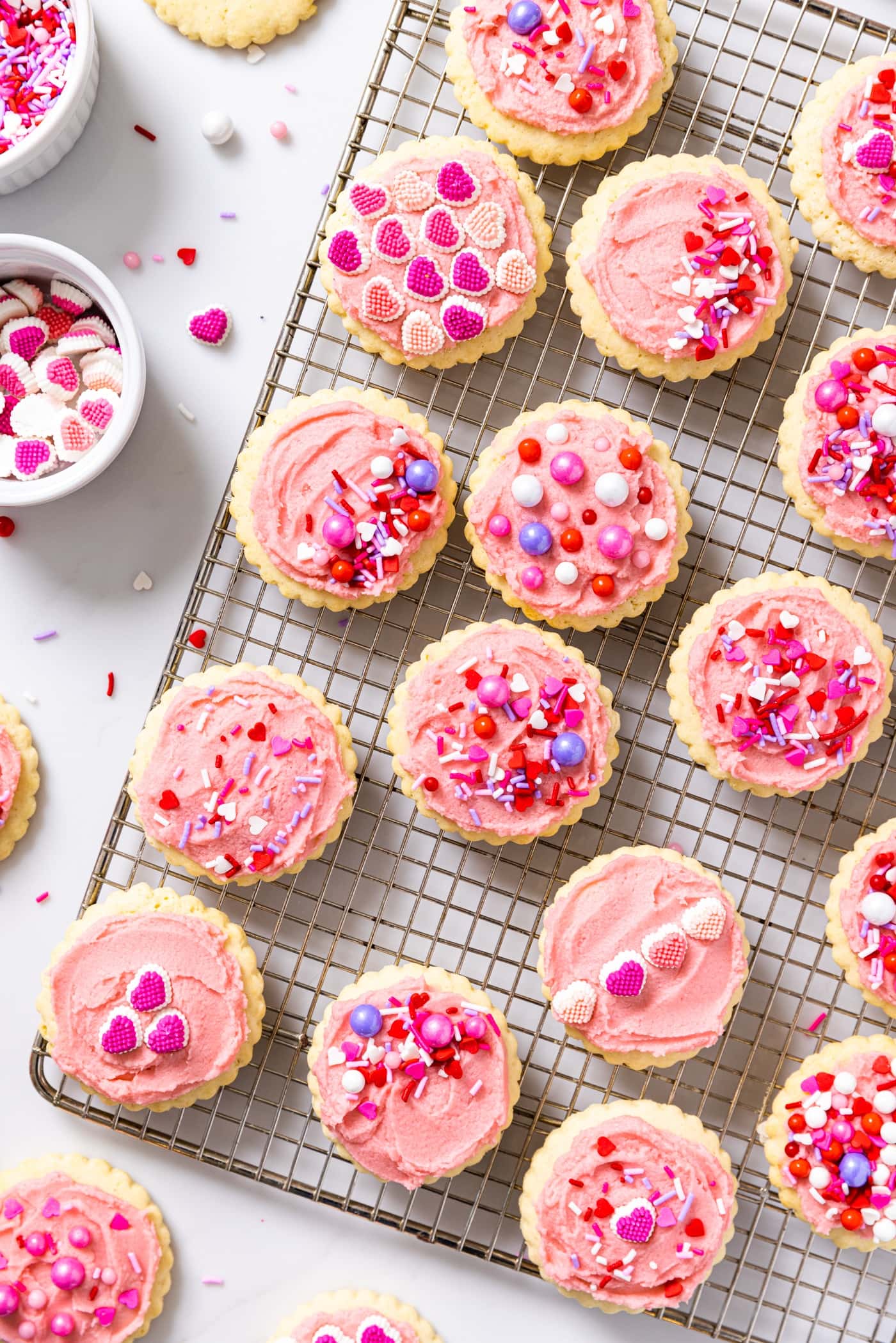 Top down view of sugar cookies sitting on baking rack with pink frosting and sprinkles all over the top