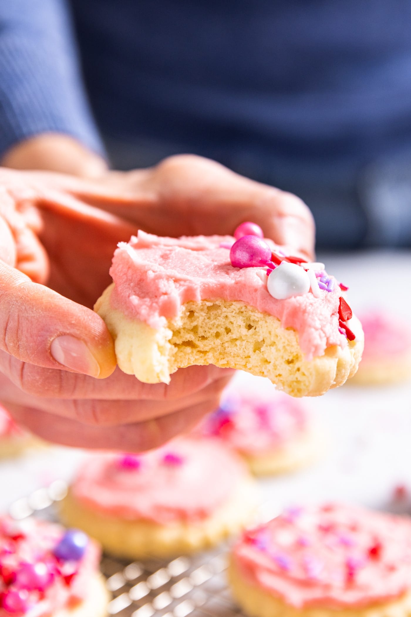 Hand holding sugar cookie with pink frosting and sprinkles on top with a bite taken out