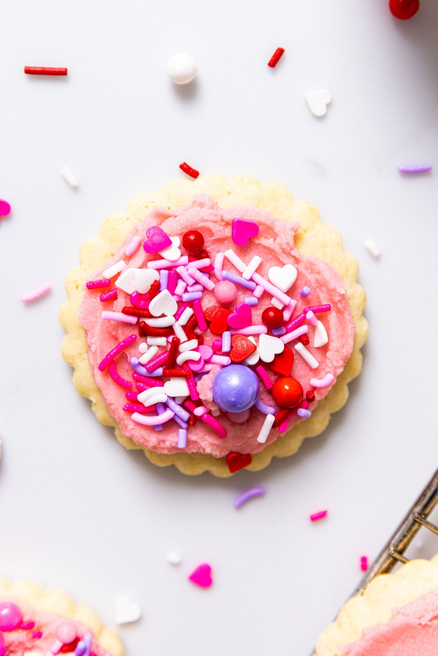 Top down view of white countertop with one sugar cookie topped with lots of sprinkles and pink frosting