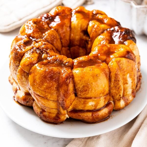 White plate with brown colored monkey bread with golden sauce all over the top all on marble surface.