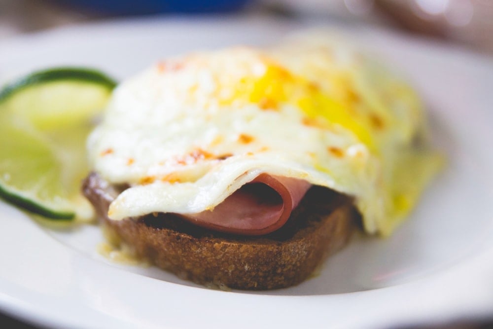 Side of Croque Madame sitting on white plate with lime wedge in background