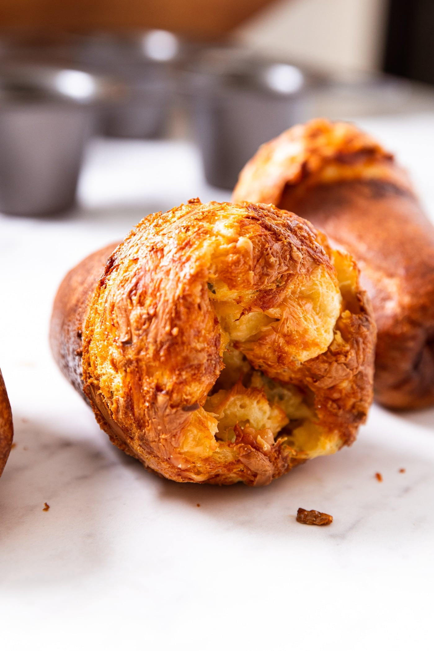 Baked popover sitting on its side on marble surface showing interior texture of popover with crispy browned top.