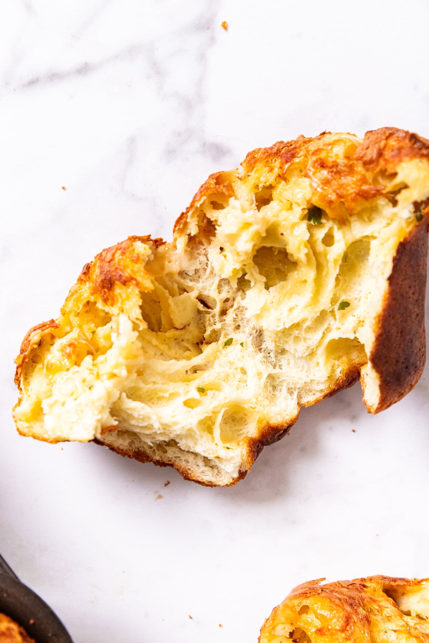 Marble surface with popover ripped in half showing the interior texture with doughy texture with bits of herbs.