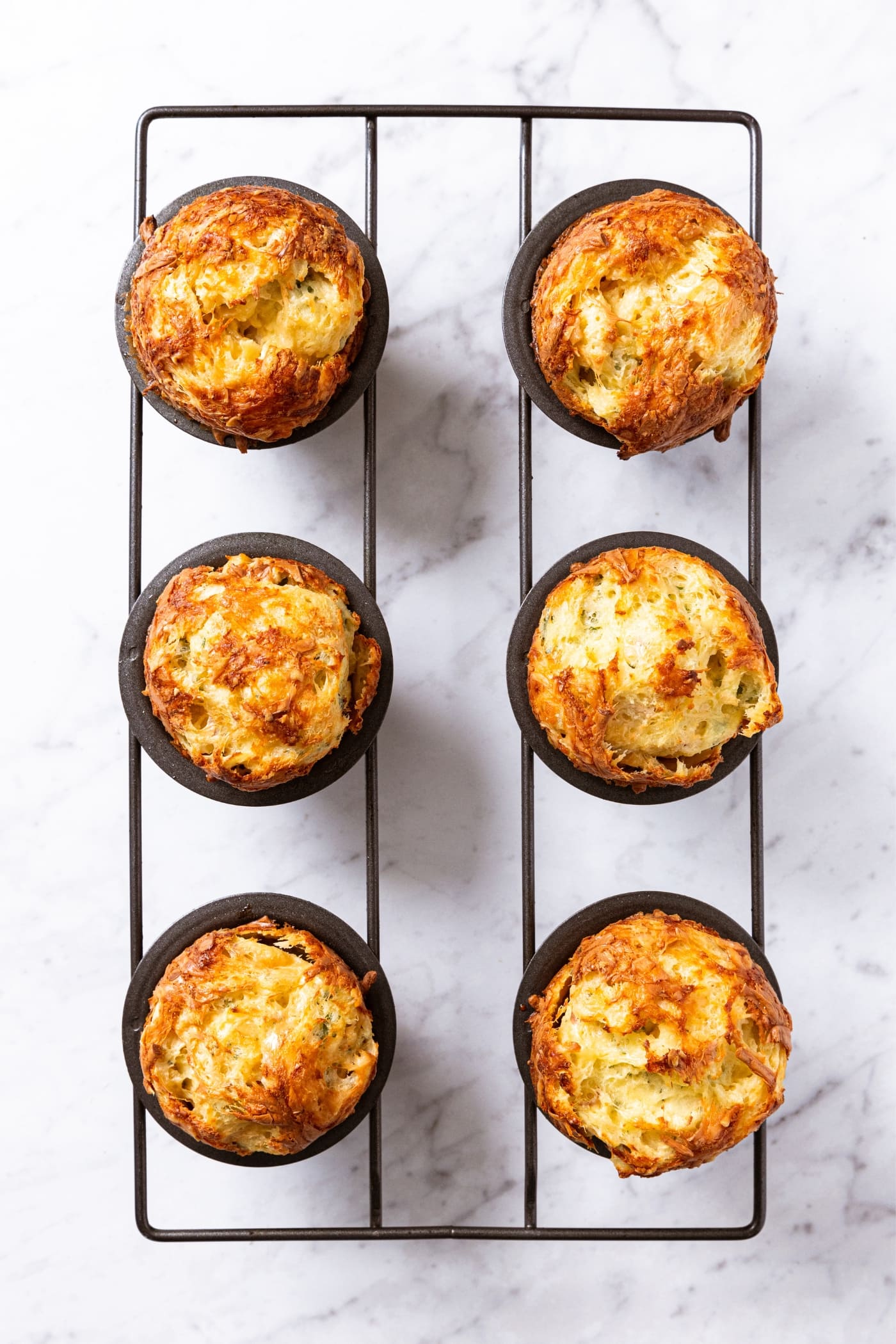 Popover pan sitting on marble surface with baked popovers in each part of the pan.