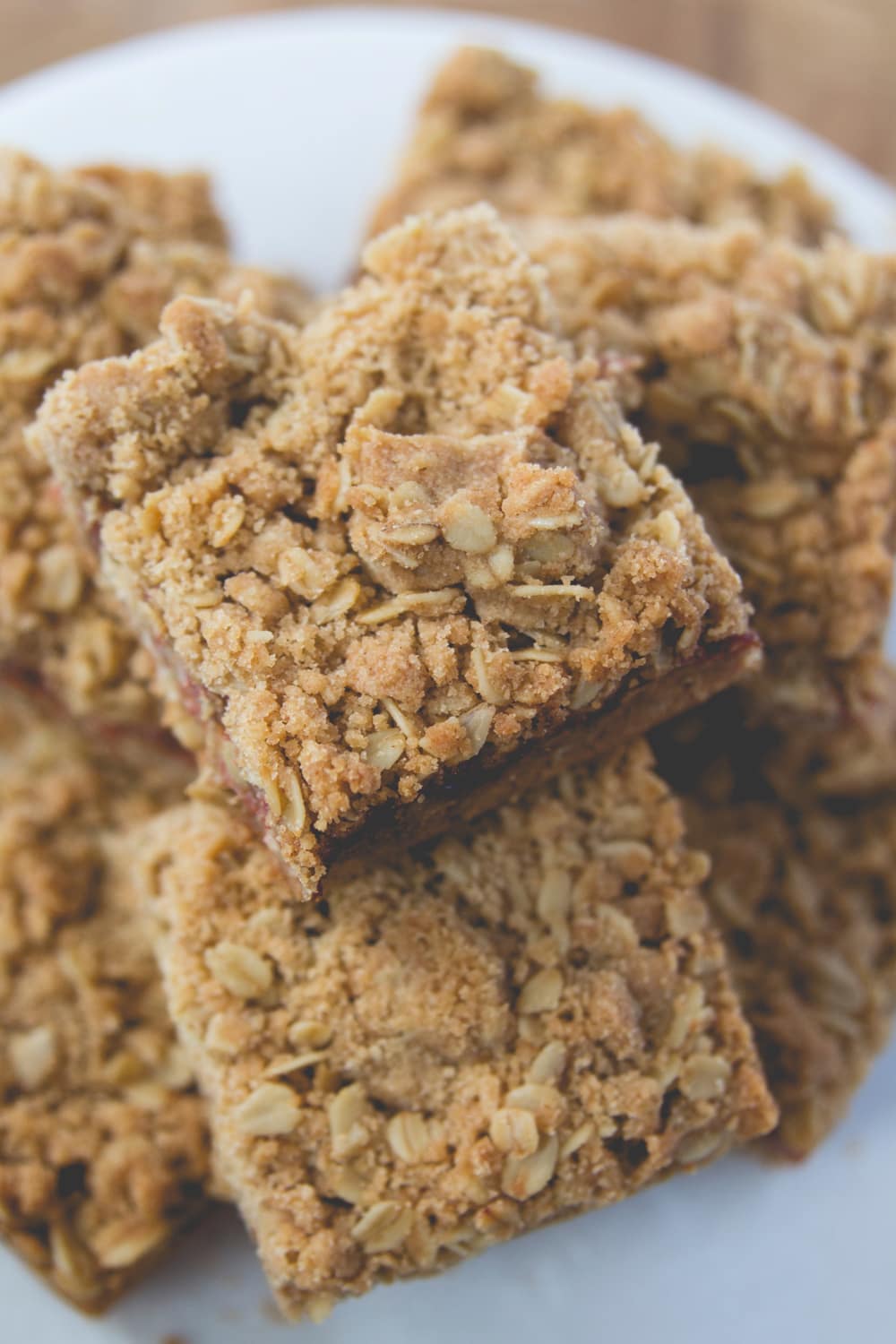 Stacks of rhubarb crumb bars sitting on white cake plate showing the crumble topping on top