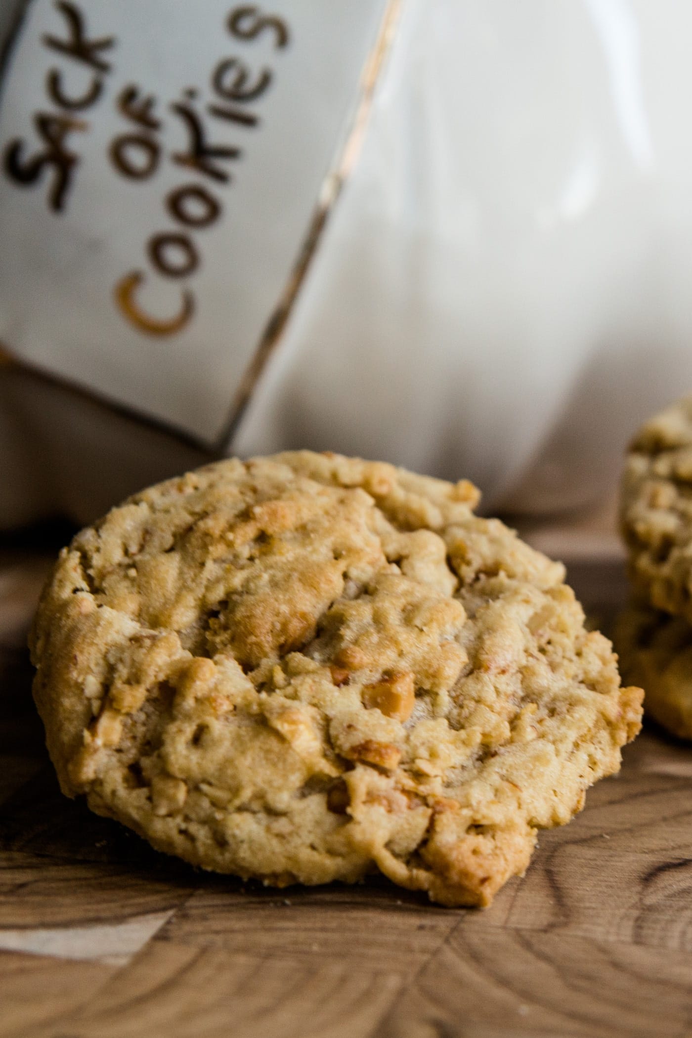 Light brown crunchy peanut cookies sitting on a wood cutting board with a sack of cookies cookie pot in background