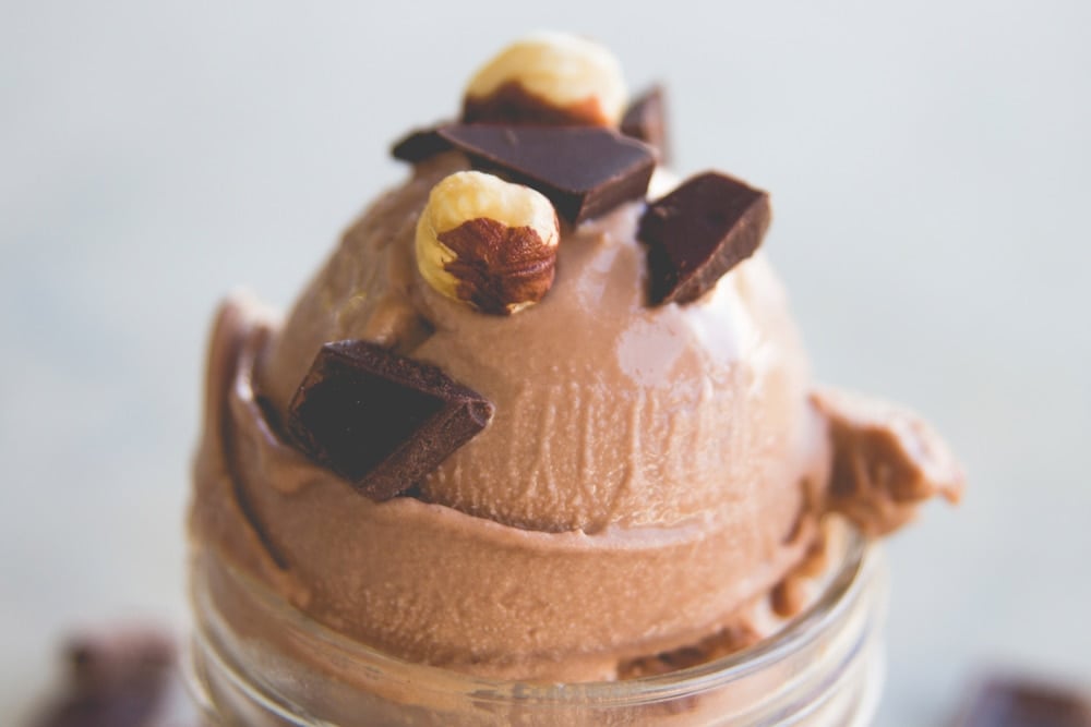 Nutella flavored ice cream topped with nuts and chocolate pieces in a small canning jar sitting on a piece of marble