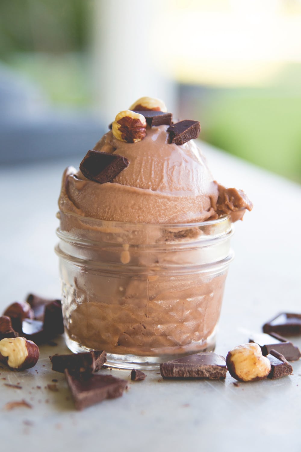 Nutella flavored ice cream topped with nuts and chocolate pieces in a small canning jar sitting on a piece of marble with greenery in the background