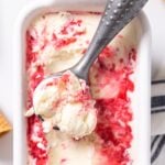 Top down view of white container sitting on white countertop with white ice cream swirled with raspberry sauce with empty ice cream cones