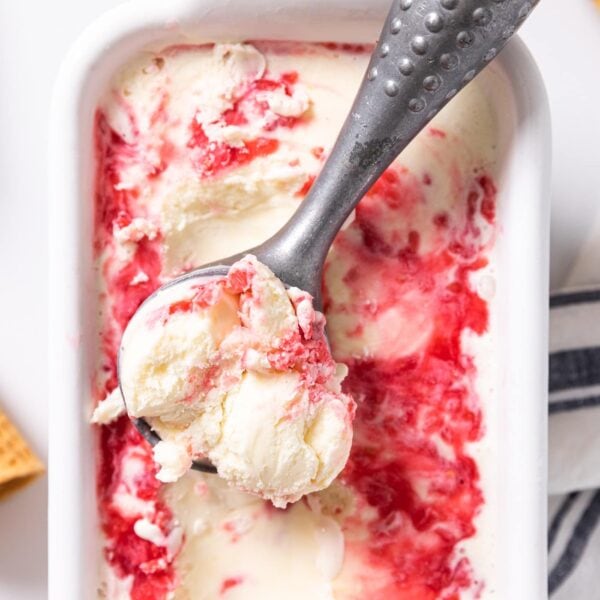 Top down view of white container sitting on white countertop with white ice cream swirled with raspberry sauce with empty ice cream cones