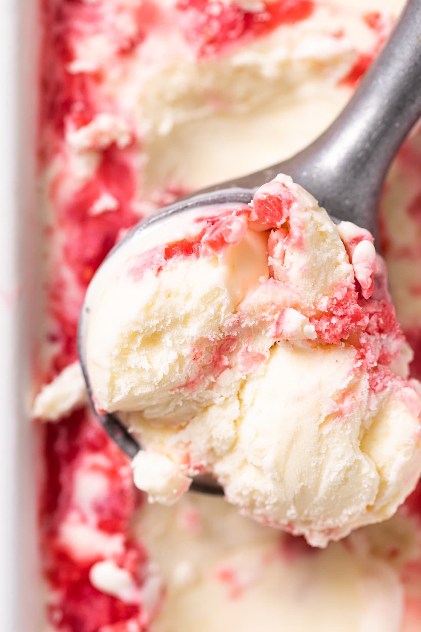 Top down view of scoop of white ice cream with raspberry swirls on top of rest of ice cream in white container