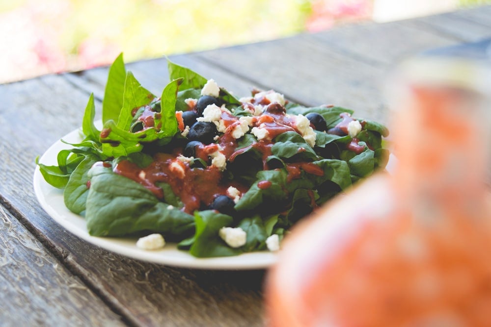 White plate filled with lettuce with blueberries and cheese and strawberry dressing on top sitting on wood table