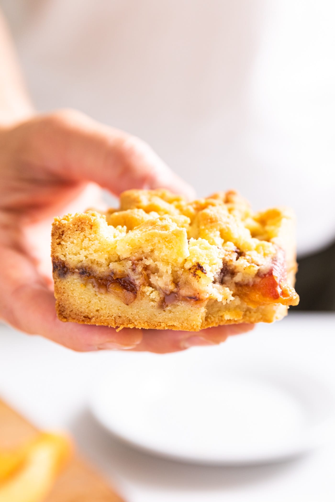 Close up side view of peach crumb bar with the three different layers exposed with hand holding the slice