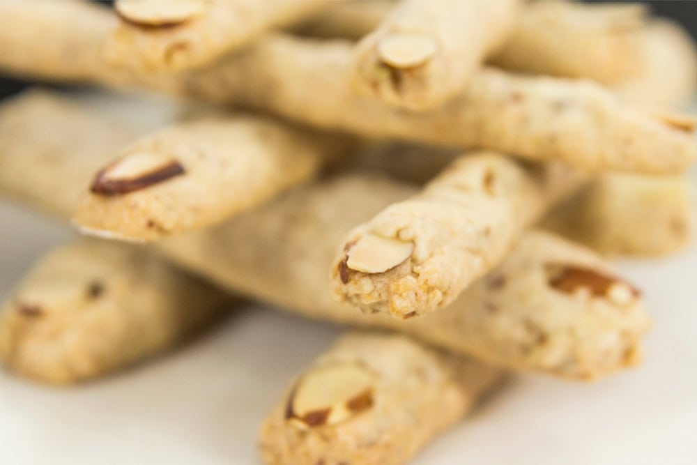 Stacked piles of finger cookies made in longer finger-like shapes with a fingernail made from an almond.