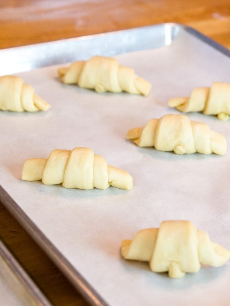 Unbaked butterhorns sitting on parchment-lined baking sheet with wooden surface in background