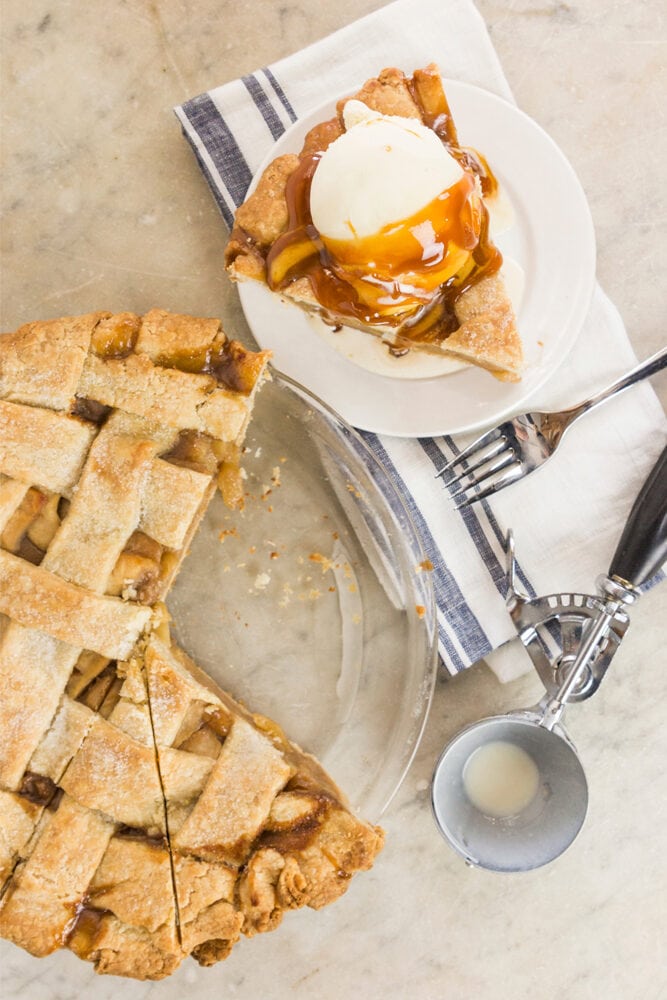 Slice of pie sitting on white plate on marble countertop with ice cream scoop and rest of pie beside