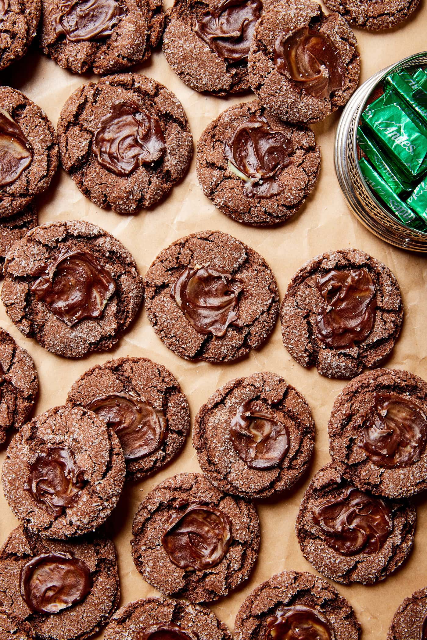 Lots of chocolate cookies with mint spread on top with bowl of Andes mints to the side.
