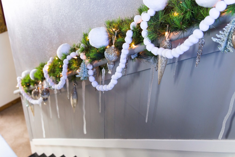 Handrail going down a staircase with green garland with white Christmas balls and silver ornaments.