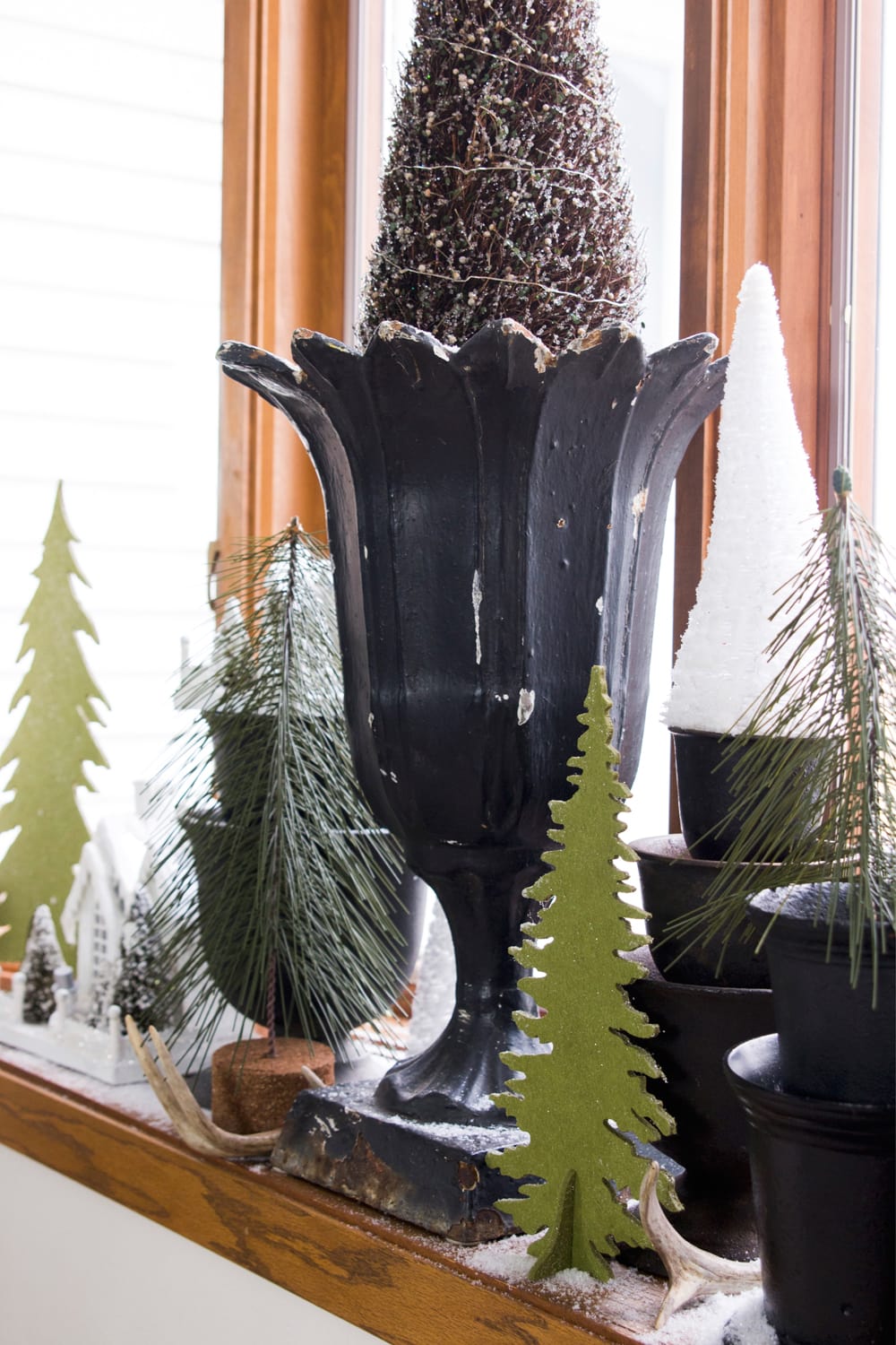 Black urn sitting on window with green cutout trees including small white trees.