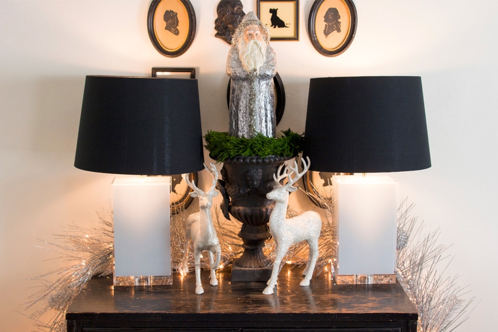 Black console table with two lamps with deer standing on surface with silver garland.