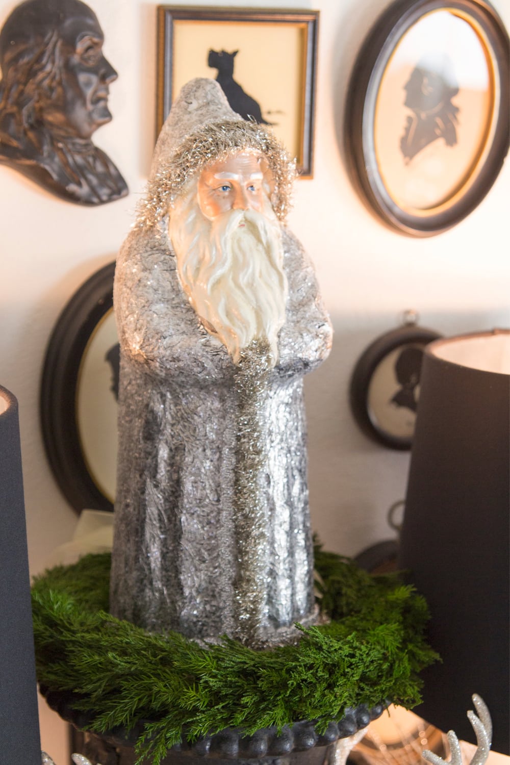 Santa with silver clothing in wreath on table with lamp to the side.