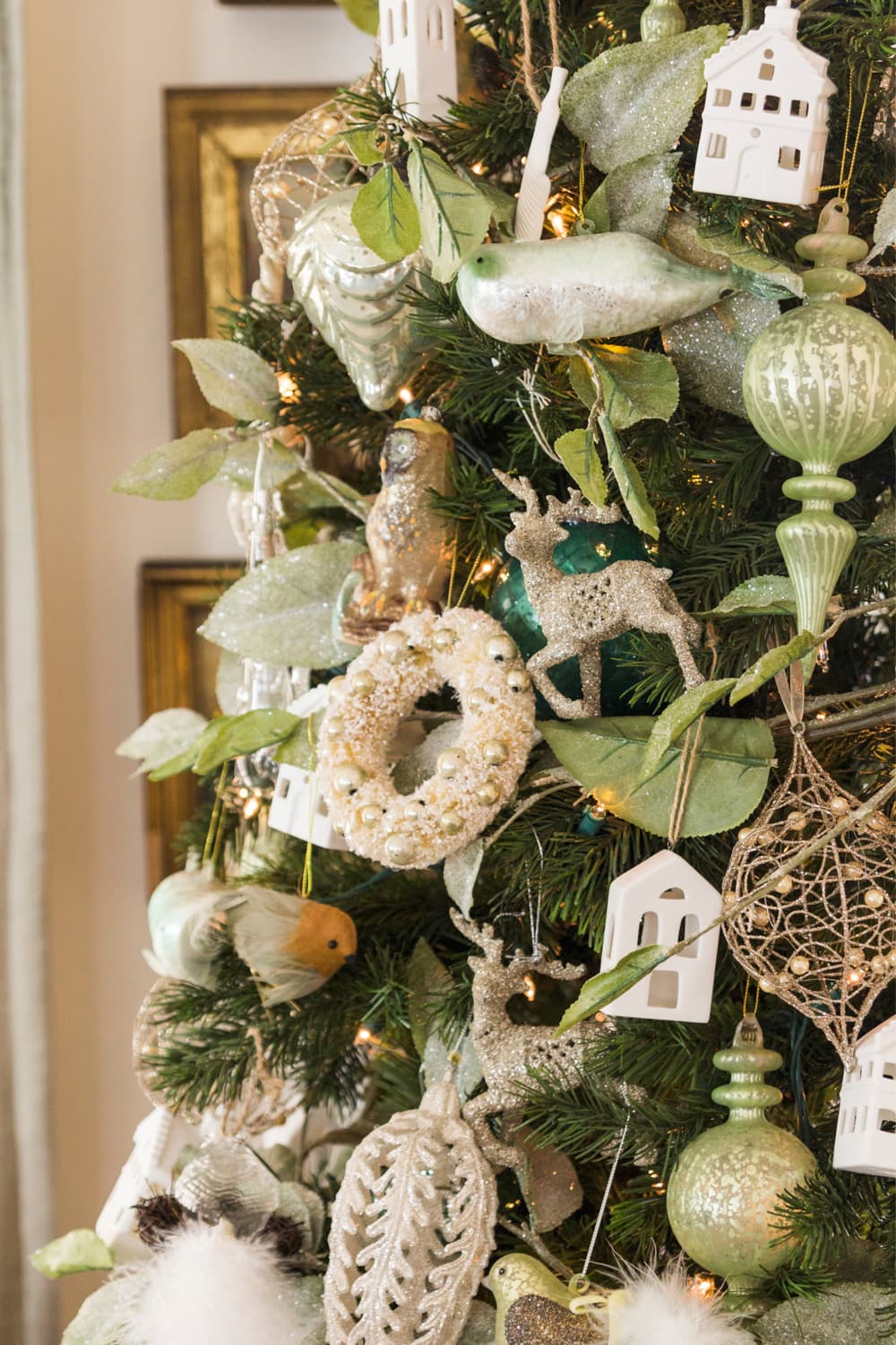 Christmas tree with silver and gold colored ornaments including wreaths, deer, and small houses.