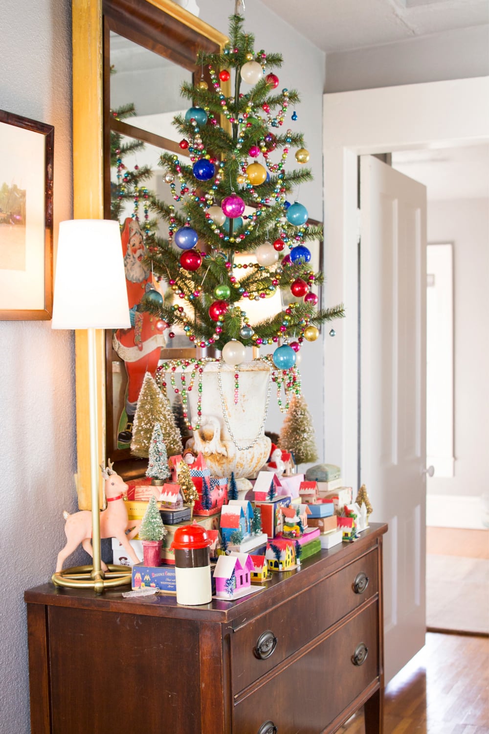 Hallway in an upstairs with table with mirror and Christmas decor piled on top of it including a tree and small Christmas boxes.