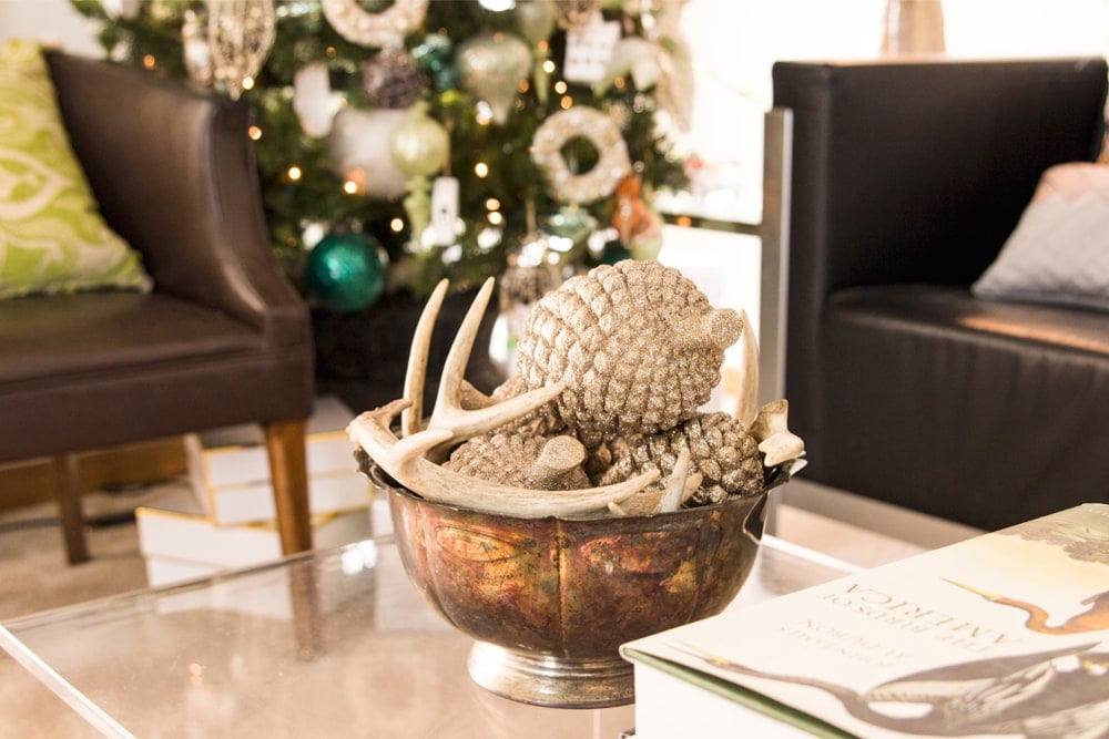 Metal bowl filled with silver ornaments and antlers on lucite coffee table in a living room.